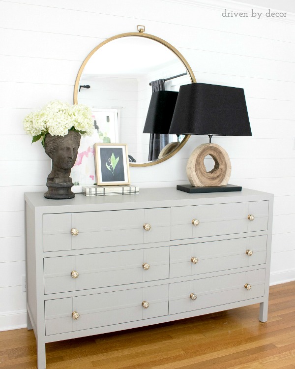 Bedroom dresser with round mirror, layered art, and bust planter filled with summer hydrangeas
