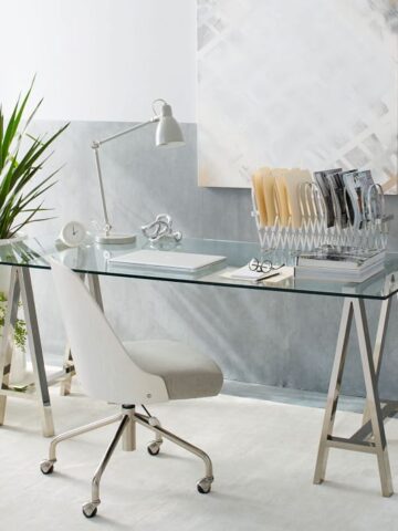 A stunning glass desk with polished nickel sawhorse legs