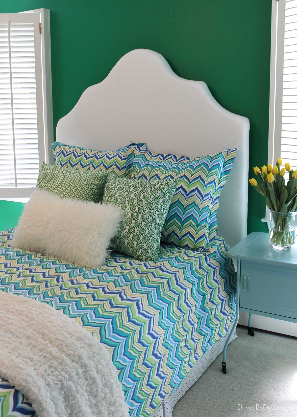 Finished DIY upholstered bed in bedroom with green, blue, and yellow bedding