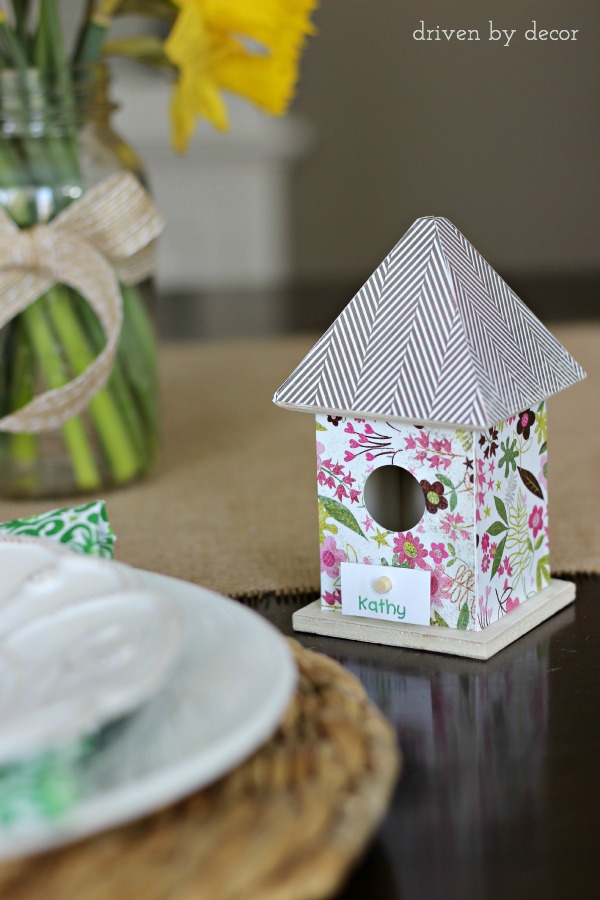 Dollar bin birdhouse covered with scrapbook paper holds name card for Easter table