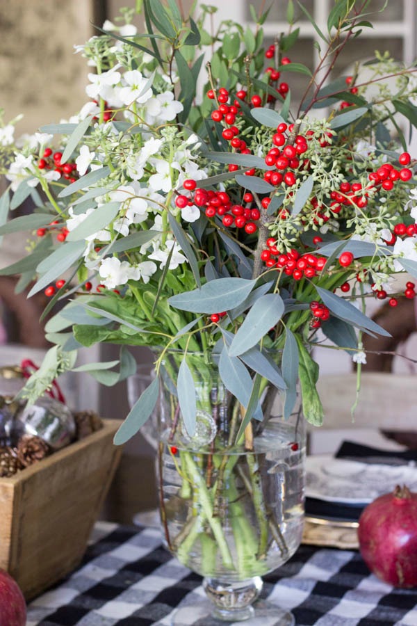 A mix of white flowers, red berries, and eucalyptus make up this festive holiday table floral centerpiece