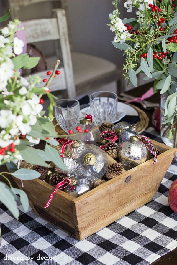 Holiday centerpiece of glass and metallic ornaments mixed with pine cones