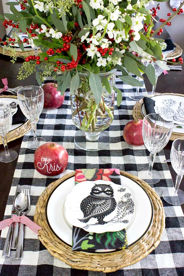 Holiday placesetting with floral centerpiece, pomegranate place cards, silverware tied with ribbon, buffalo check runner, and festive plates