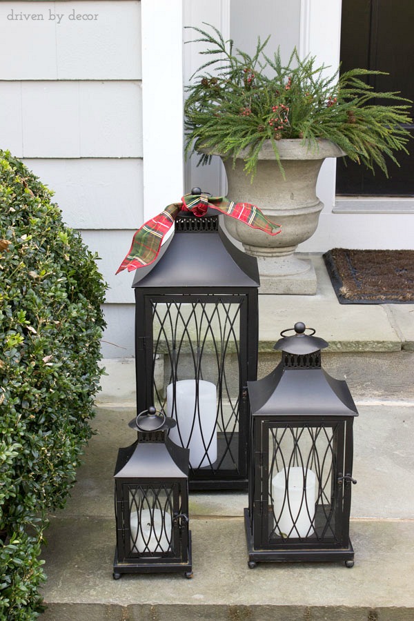 Simple holiday decorations for your front porch - a set of lanterns adorned with holiday ribbon and urns filled with greenery and berries