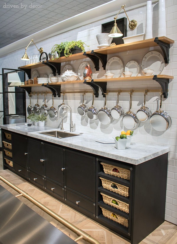 Fabulous La Cornue kitchen with open shelving, brass pot rack, swing-arm sconces, and cabinets with pull-out baskets