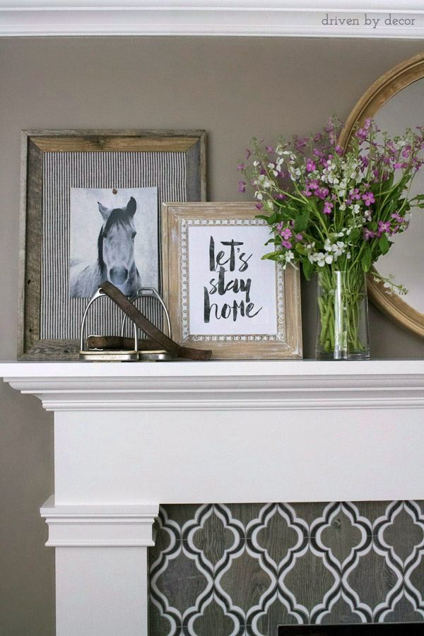 Loving this arrangement of art on the fireplace mantel with a round mirror in the middle and layered, framed art and flowers