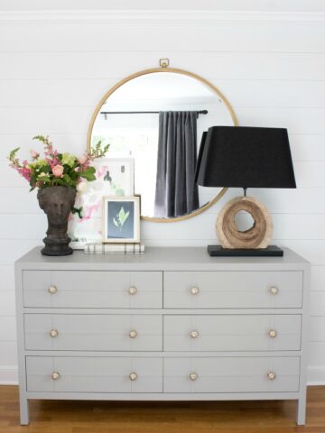 Simple styling over a bedroom dresser - large round mirror, lamp, and planter with two pieces of layered art