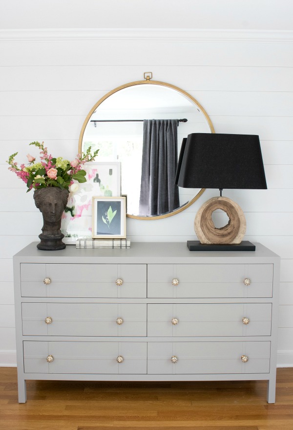 Simple styling over a bedroom dresser - large round mirror, lamp, and planter with two pieces of layered art