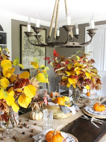 Vases filled with fall branches, scattered acorns, and a wood bowl filled with mini pumpkins were used to create a simple, natural fall tablescape