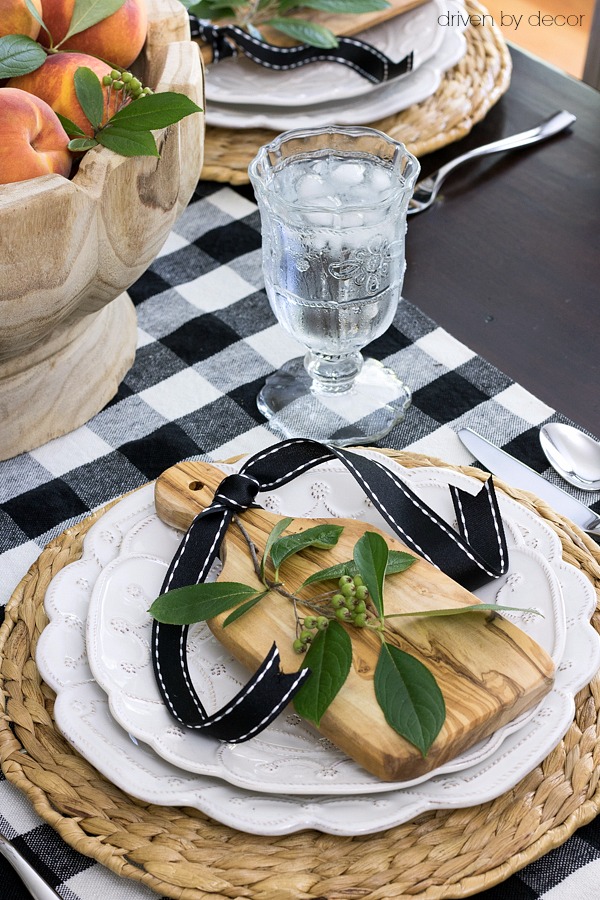 Fall place setting with mini cutting boards, ribbon, and a sprig of greenery on plates with woven chargers.