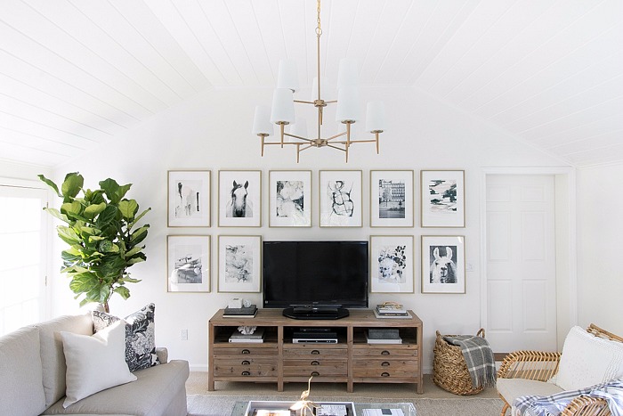 family-room-with-art-wall-surrounding-tv-two-tiered-chandelier-neutral-sectional-rattan-accent-chair-and-acrylic-coffee-table