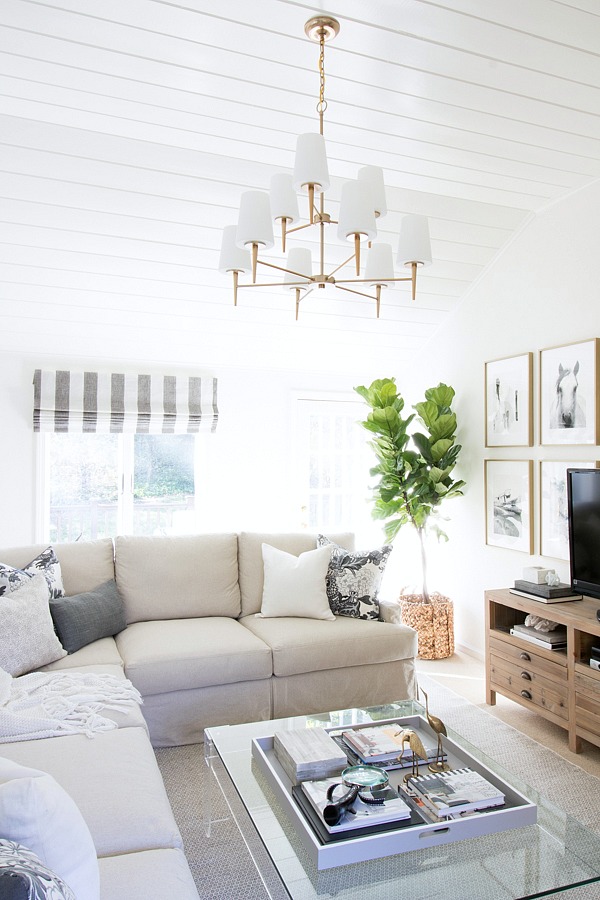 Family room in neutrals with slipcovered sectional, acrylic coffee table, and two-tiered chandelier