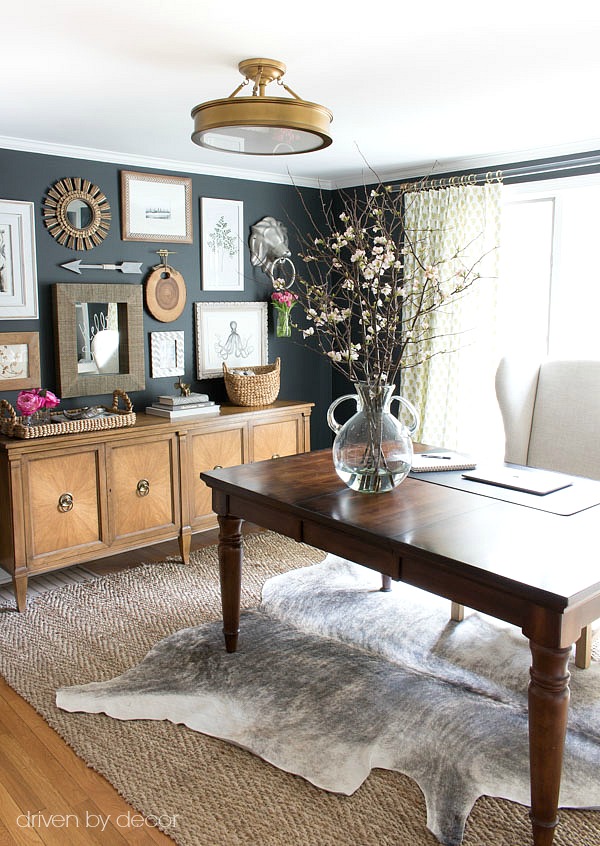 Home office with layered rugs (jute and cowhide) and eclectic art gallery against charcoal walls