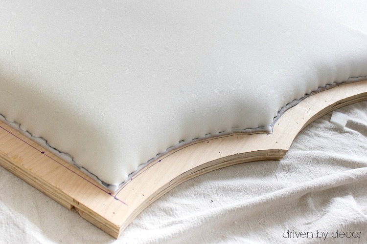 Stapling edges of foam onto plywood headboard in preparation for upholstery and nailheads