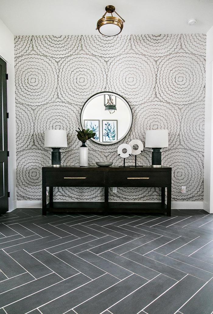 Stunning entry designed by Sita Montgomery Interiors with black herringbone floors and a long console with twin lamps and a round mirror.