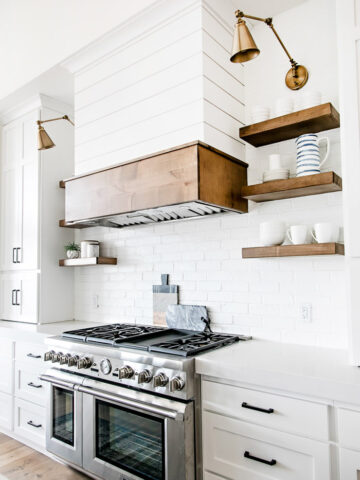 White modern farmhouse kitchen with shiplap range hood, open wood shelving, and swing arm sconces - Sita Montgomery Interiors