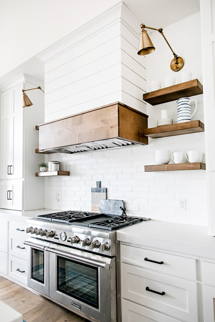 White modern farmhouse kitchen with shiplap range hood, open wood shelving, and swing arm sconces - Sita Montgomery Interiors