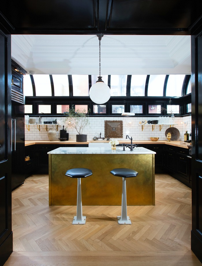 Gorgeous kitchen with herringbone wood floors, black cabinets, butcher block countertops, and gold island