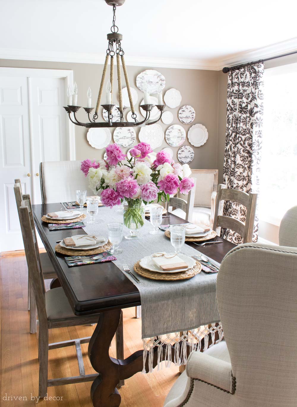 Classic dining room with dark gray walls, rope chandelier, ladder back side chairs, wingback end chairs, and decorative plate wall