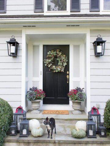 Our fall front porch with black lantern sconces, fall wreath, and planters filled with cabbages, kale, and mums. Part of a New England fall home tour!