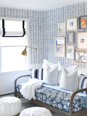Blue and white bonus room area with daybed, blue floral quilt, blue and white pillows, white leather Moroccan poufs, Roman shades, and an art gallery wall!