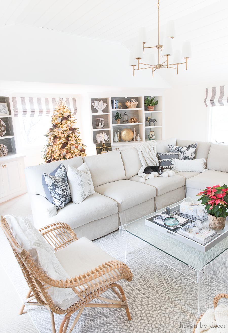 Love this cozy family room decorated for Christmas! Includes two-tiered chandelier, sectional, rattan chair, acrylic coffee table, and more!