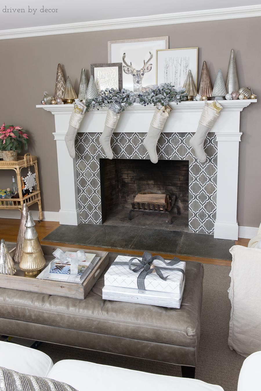 Our fireplace mantel decorated for the holidays with flocked greenery, metallic Christmas trees, layered art, and linen stockings
