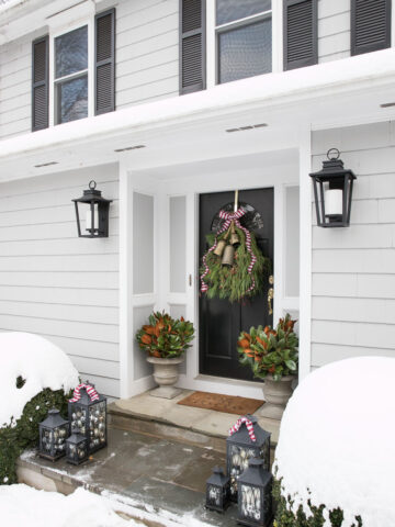 Our front porch decorated for Christmas with lanterns filled with ornaments, magnolia branches in our planters, and a greenery swag with bells! Perfect for Christmas!