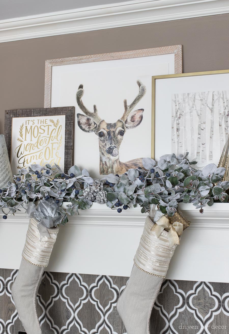 Fireplace mantel decorated for Christmas with layered art and faux frosted eucalyptus branches