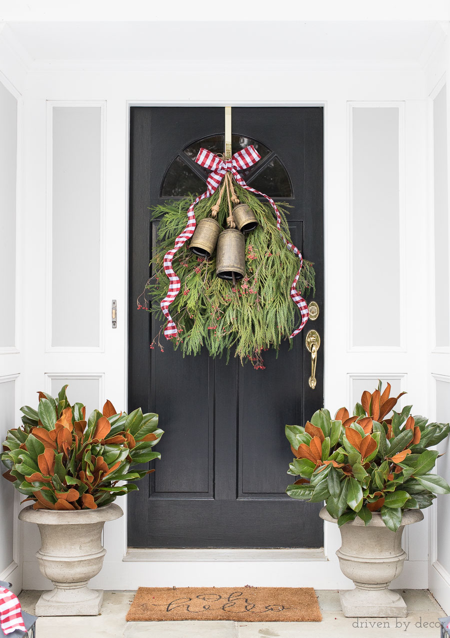 Our front porch decorated for Christmas with a greenery swag topped with bells and ribbon and planters filled with magnolia branches