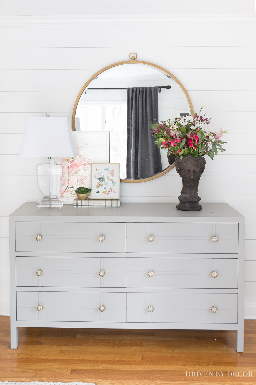 Gray bedroom dresser, large round mirror, and acrylic lamp - perfect for a bedroom!