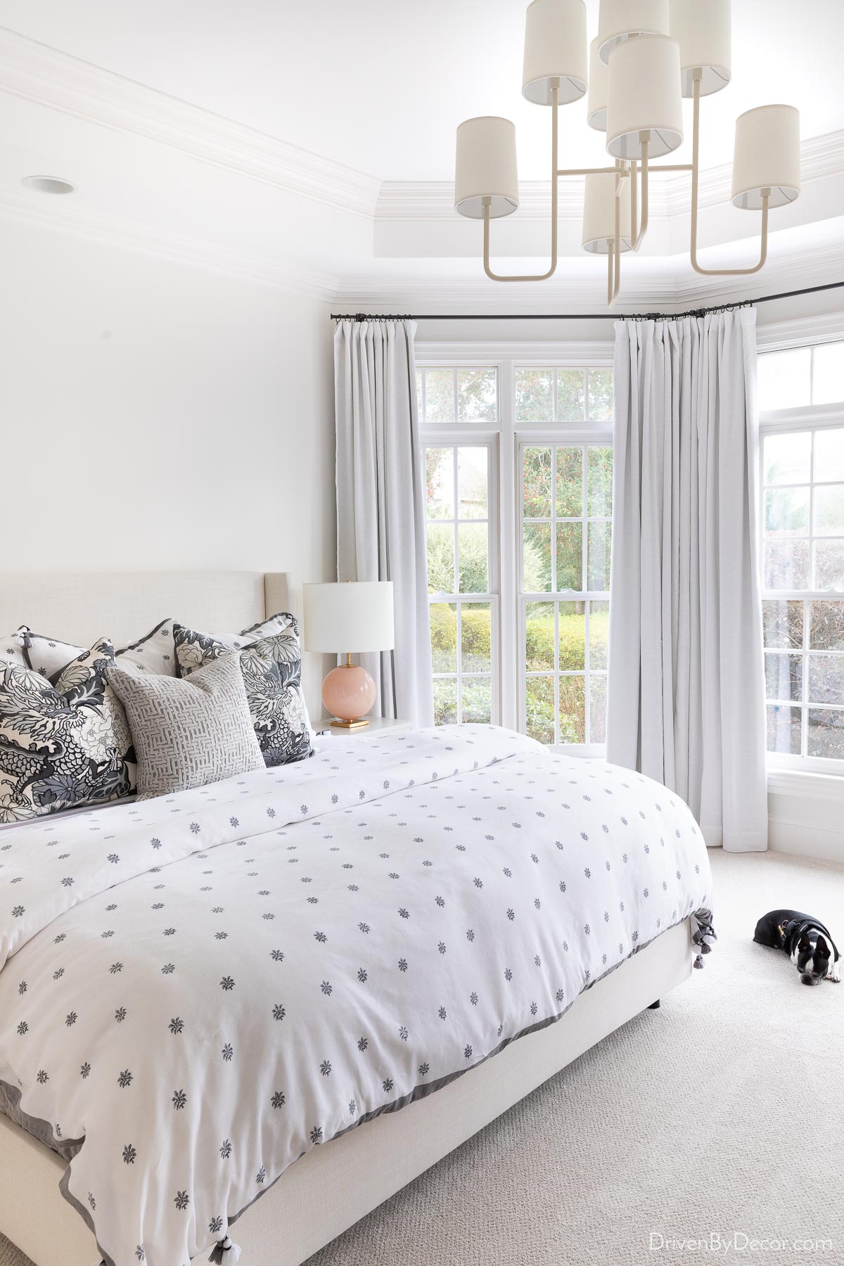 Guest room bedding in shades of gray in bedroom with tall windows and chandelier