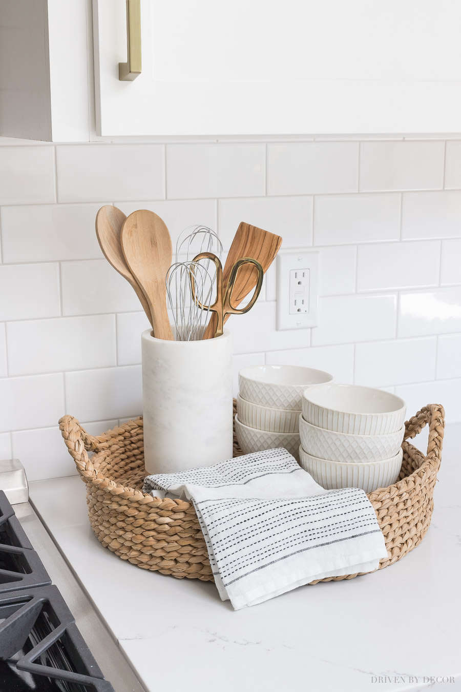 The perfect set-up for next to your range! A round woven tray holds most-used utensils in a pretty marble holder, a hand towel, and white patterned bowls!