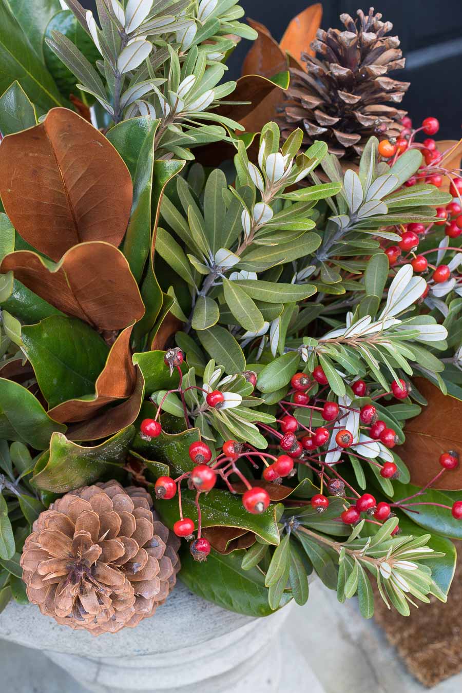 Love the mix of magnolia branches, greenery, rose hips, and pinecones in these holiday planters!