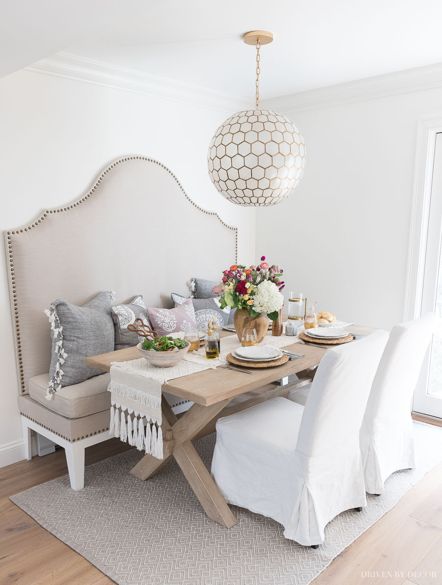 Kitchen eat-in area with tall upholstered banquette, wood table, slipcovered dining chairs, and capiz pendant