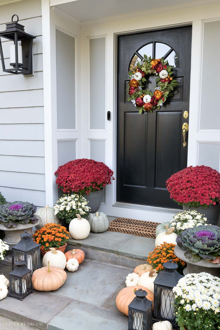 Mum, pumpkins, and lanterns line this gorgeous fall porch!