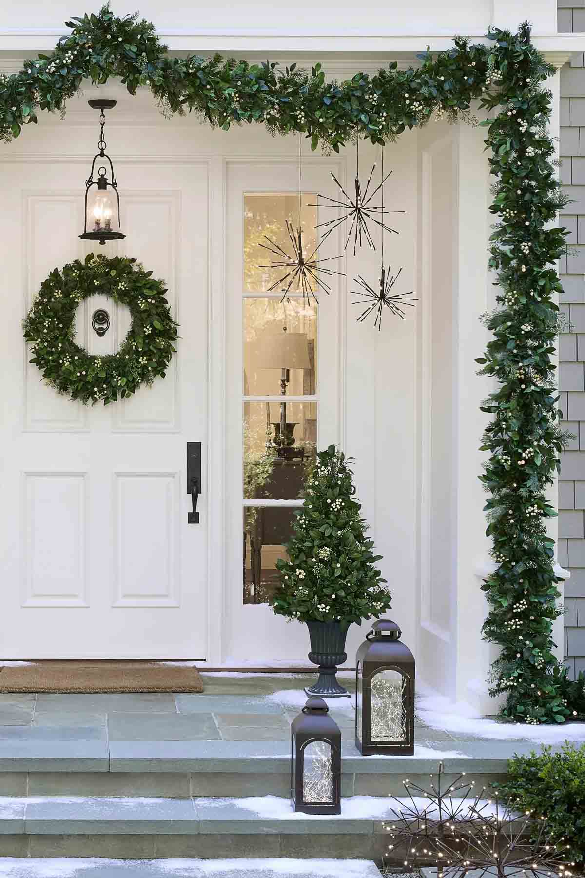 Front porch decorated for the holidays with fairy light filled lanterns