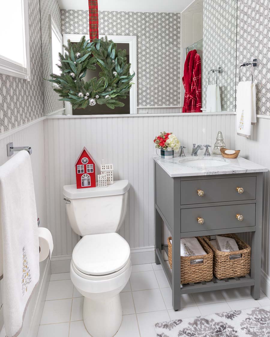 Super cute bathroom decorated for Christmas with Christmas houses and a wreath layered over the mirror!