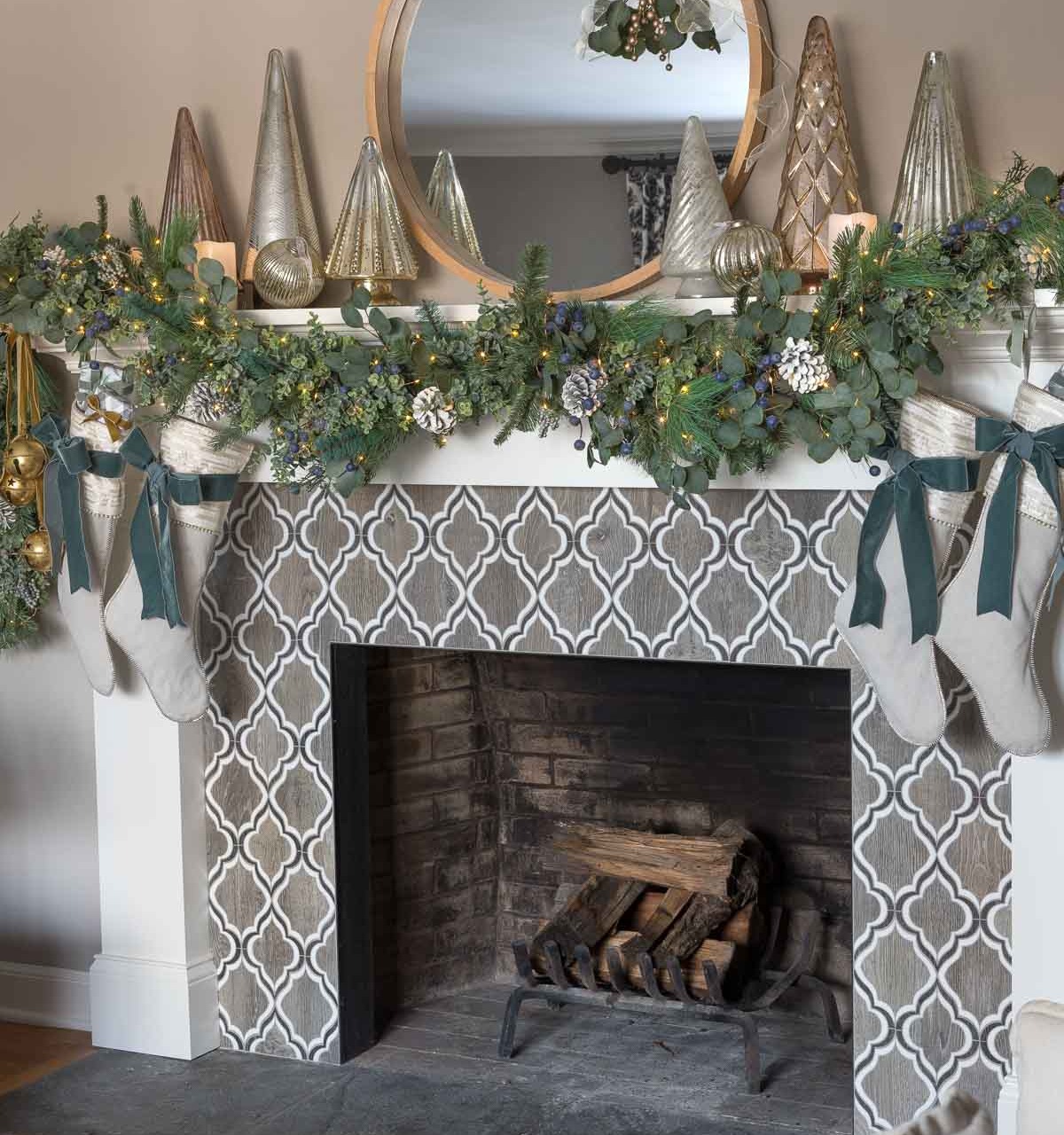 Our fireplace mantel at Christmas with greenery, mercury Christmas trees, glowing faux candles, and twinkle lights