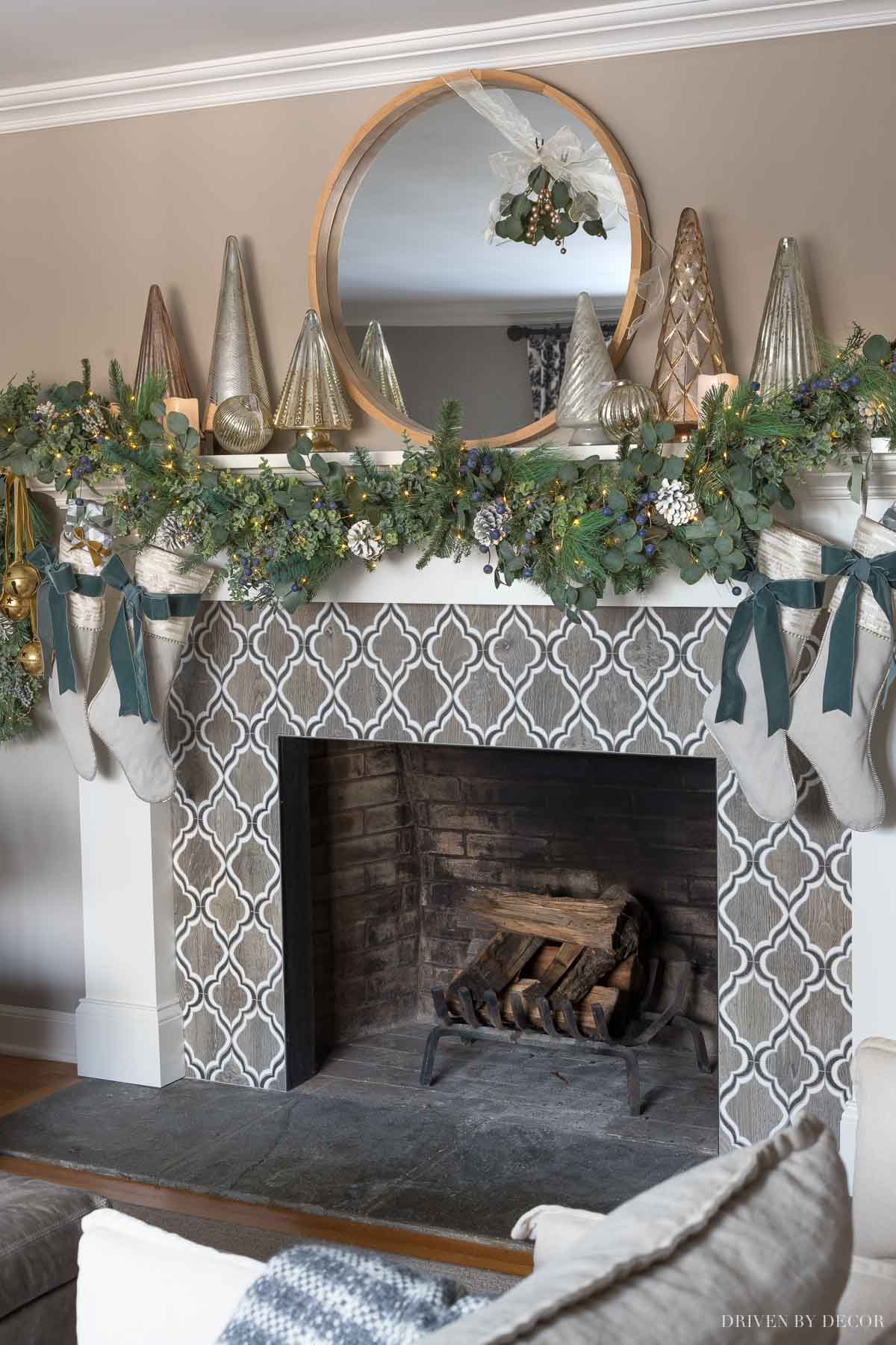 Our fireplace mantel at Christmas with greenery, mercury Christmas trees, glowing faux candles, and twinkle lights