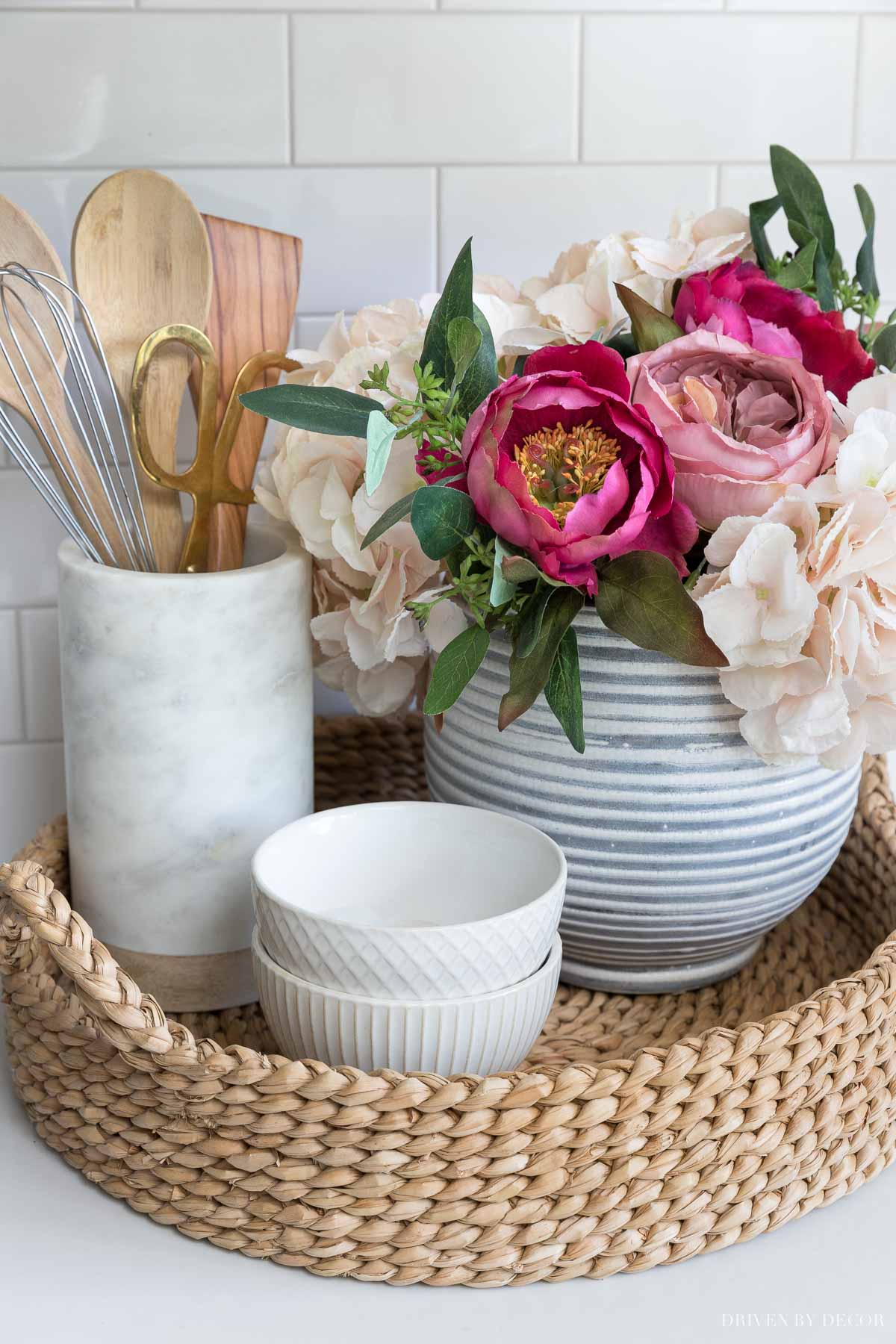 The artificial flowers in our kitchen sitting in a round woven tray