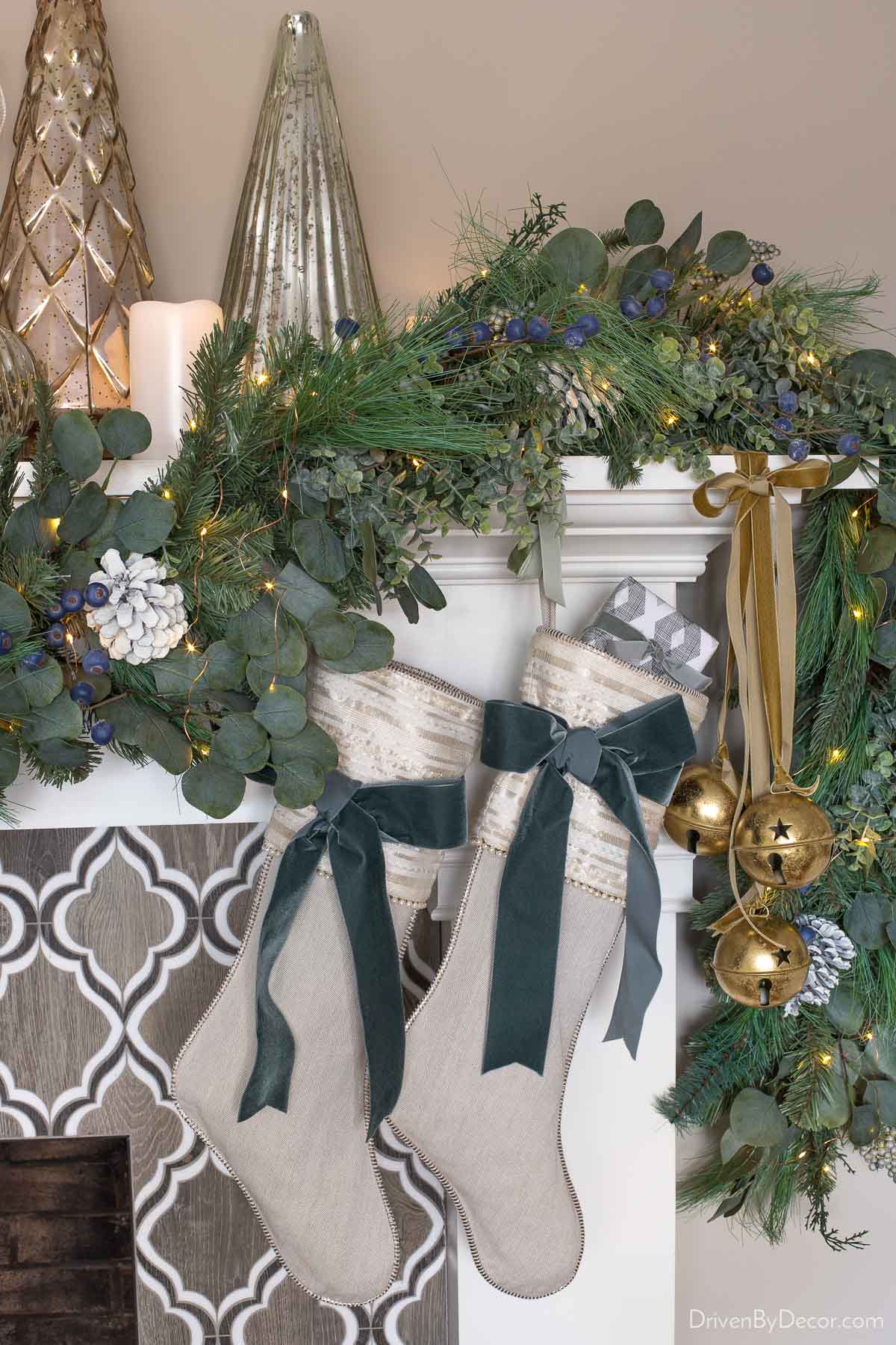 Fireplace mantel layered with greenery, metallic trees, and battery operated candles