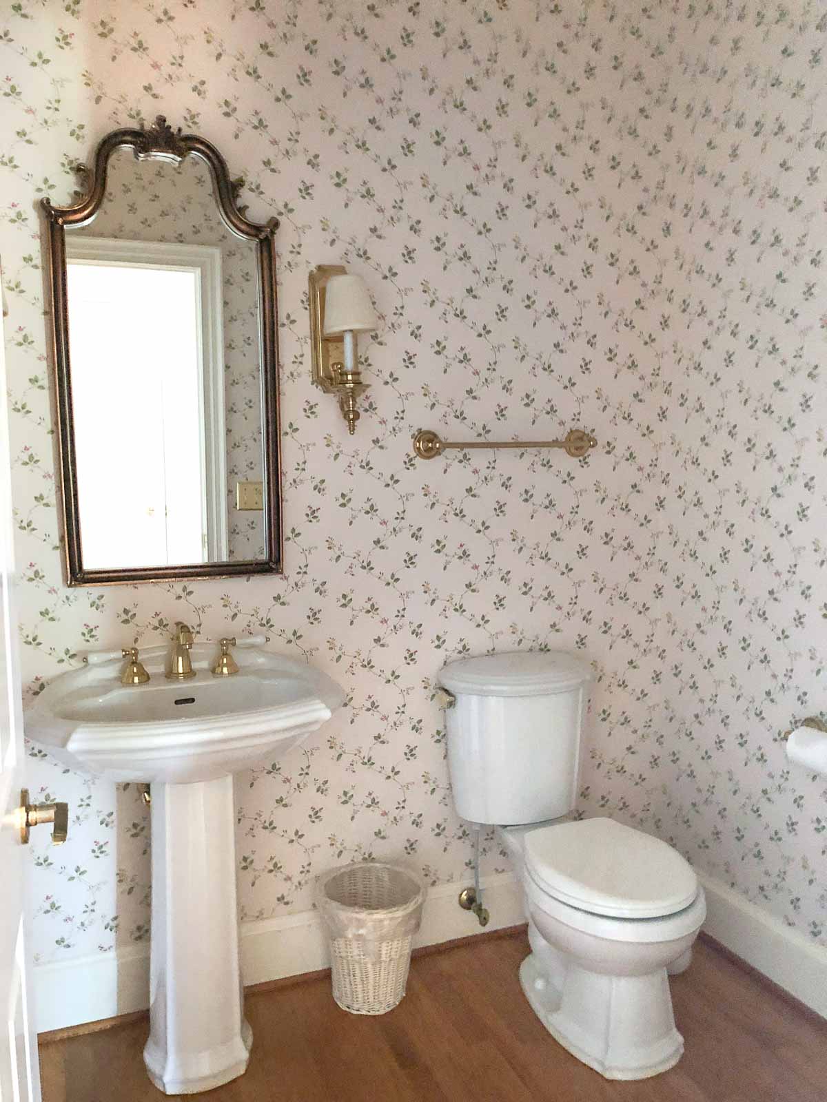 Our hall bathroom before remodeling - pedestal sink, arched mirror, and dated floral wallpaper