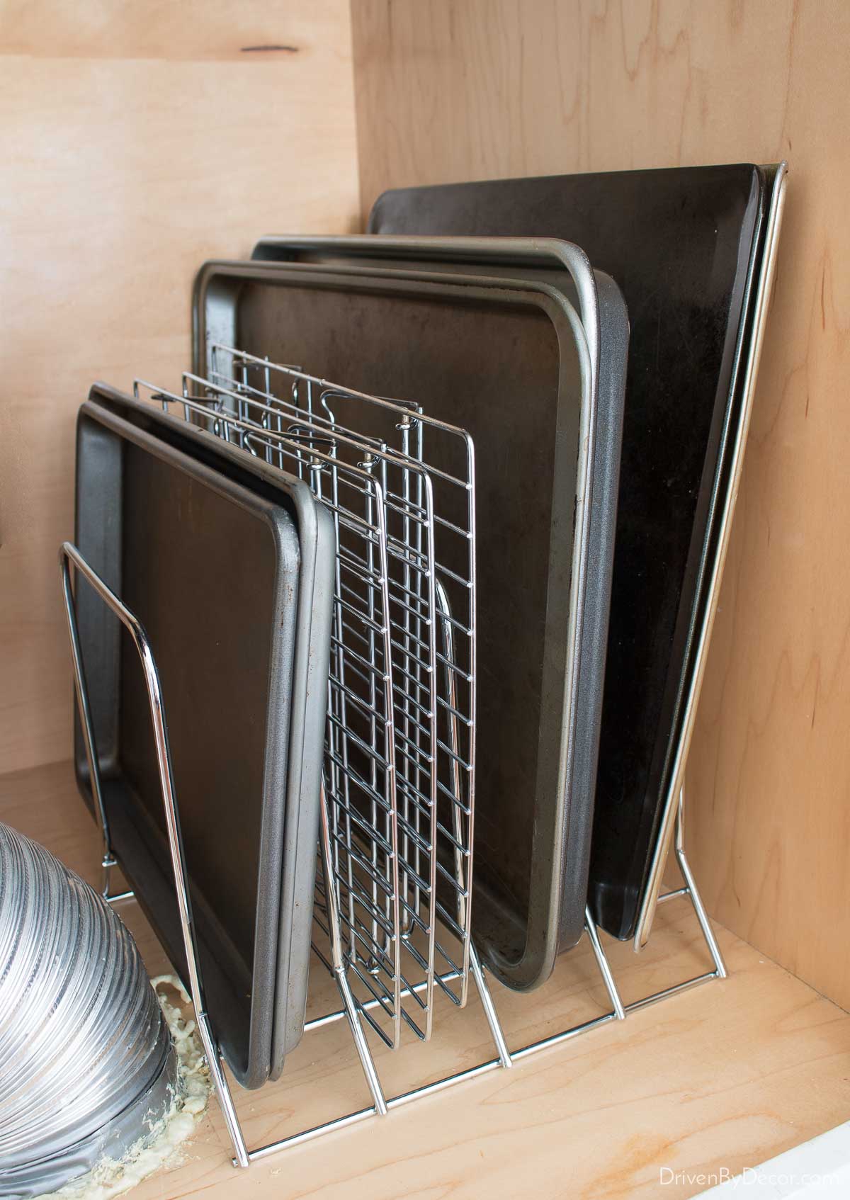 Organized baking sheets & pans on a divided metal rack in a kitchen cabinet