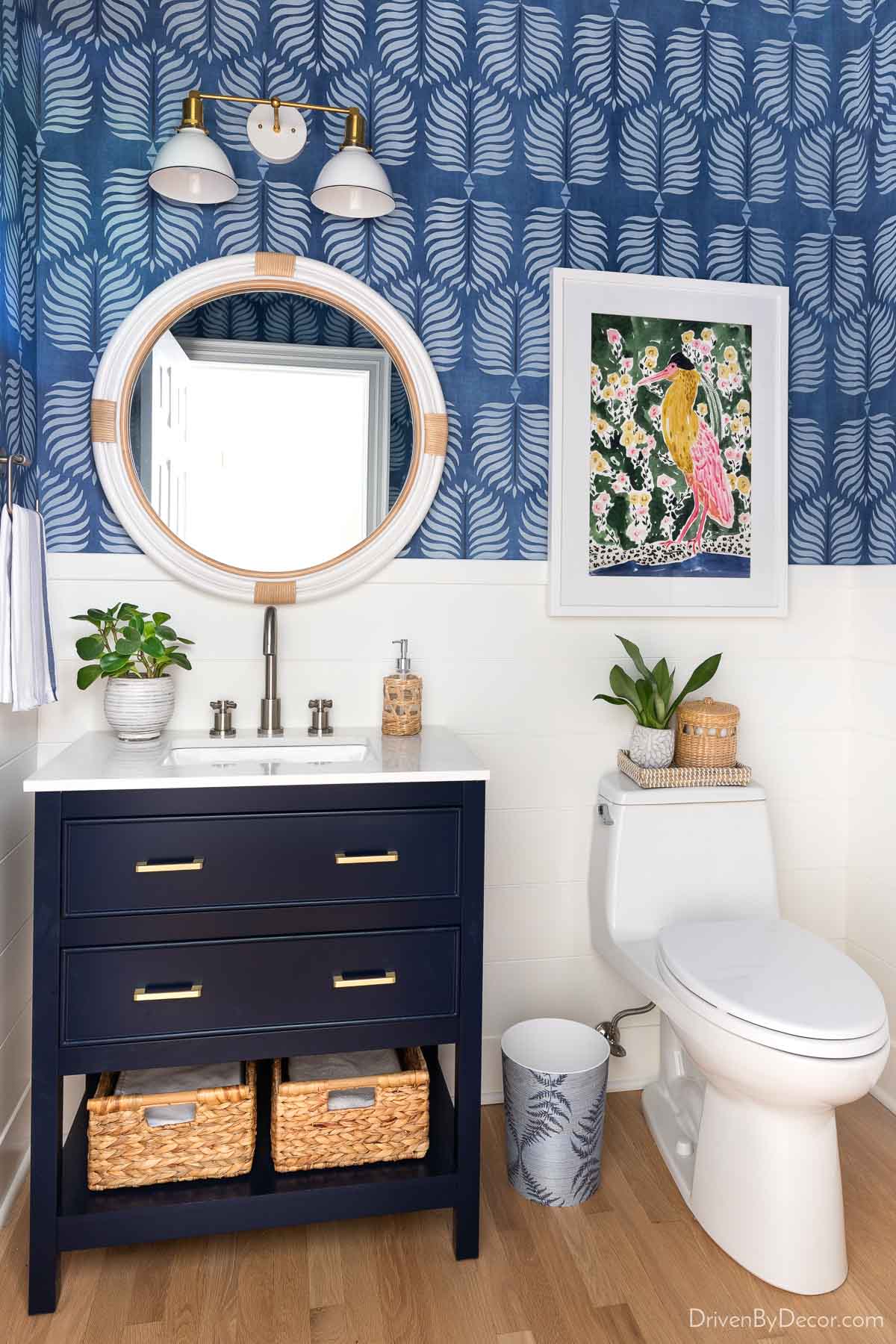 Bathroom with shiplap walls, blue wallpaper, single navy vanity, and round mirror