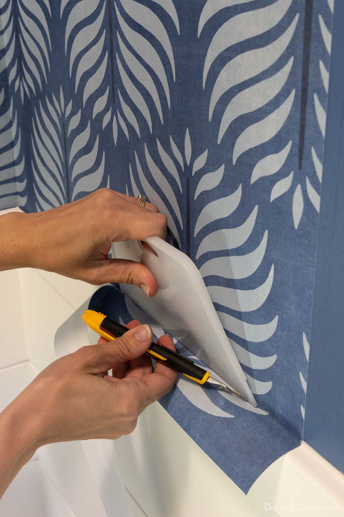 Using a straight edge and razor to cut off excess wallpaper