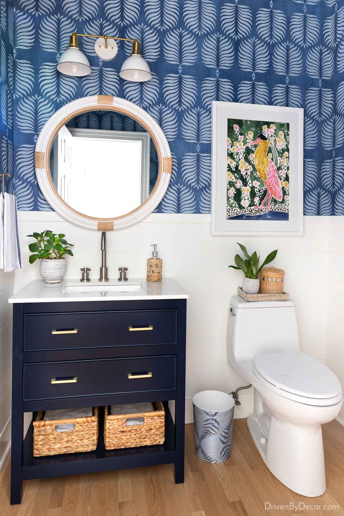 Blue bathroom with round white rattan mirror over vanity