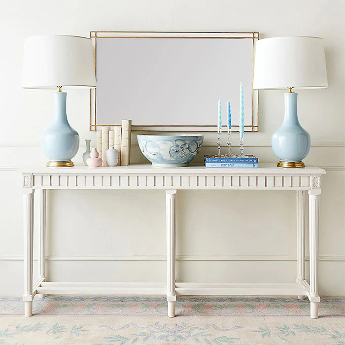Console table decor including books, lamps, and a bowl
