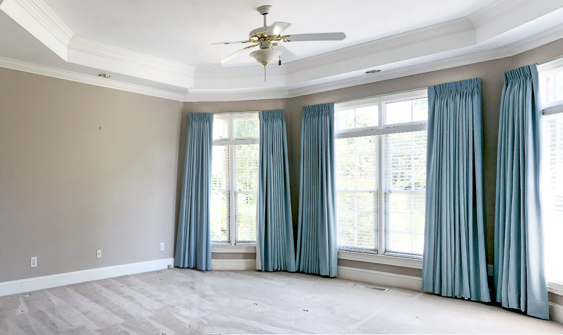 Primary bedroom before remodeling with beige walls, green curtains, and ceiling fan