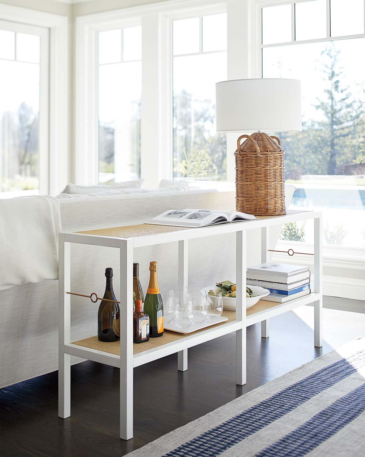 Simple white table behind sofa with raffia wrapped shelves and brass detailing